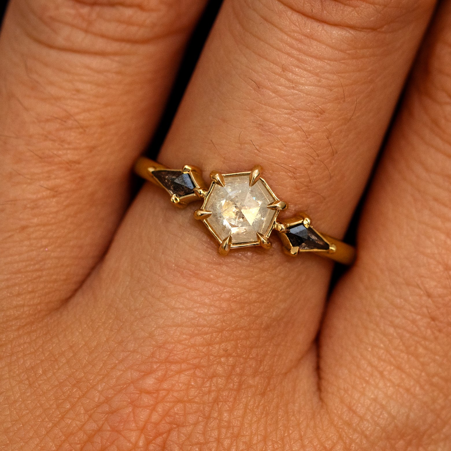 A model's hand wearing a 14k yellow gold Hexagon Salt and Pepper Diamond Black and White Ring