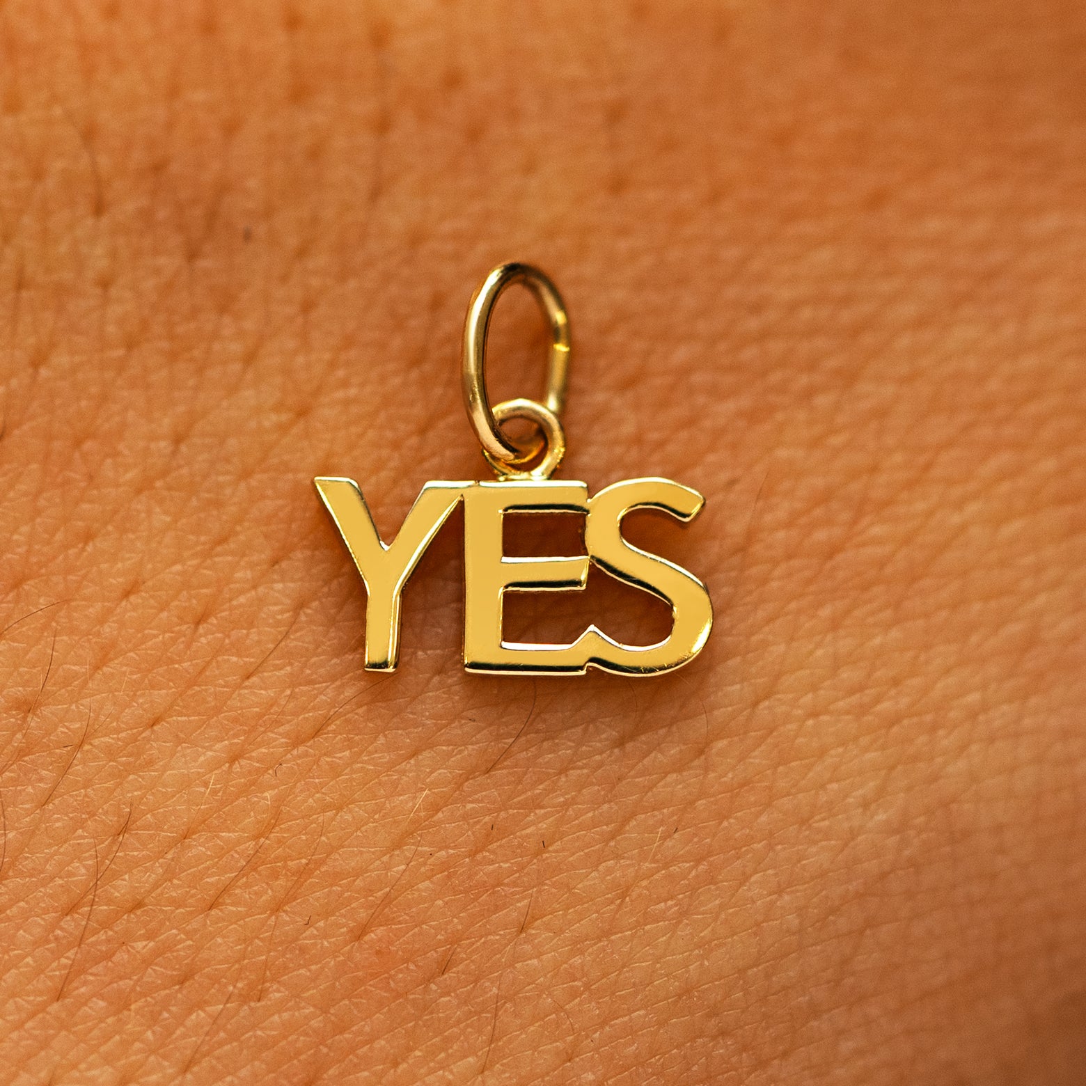 A solid 14k yellow gold Yes Charm on the back of a models hand