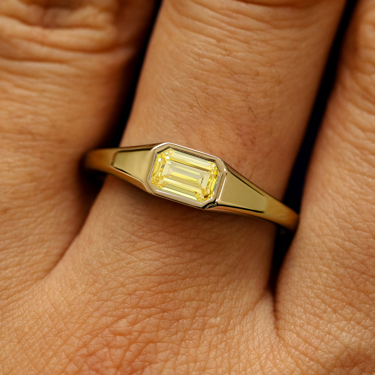 Close up view of a model's fingers wearing a 14k yellow gold emerald cut yellow lab created diamond Signet Ring