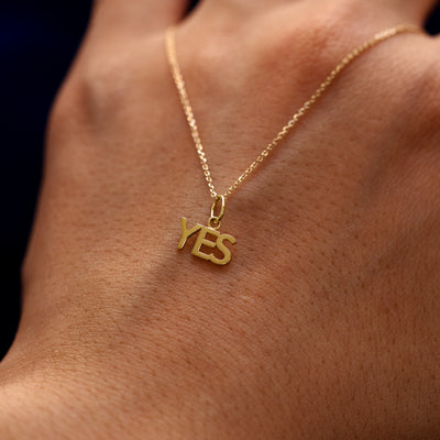 A 14k gold Yes Charm on a Cable Chain draped over the back of a models hand