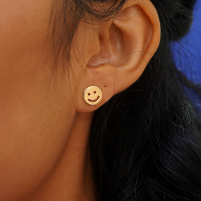 A model's ear wearing a 14k yellow gold Smiley Face Earring 